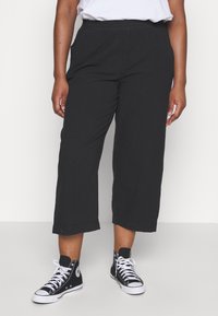 Pantalons larges noirs avec une taille élastique et des poches, associés à des baskets montantes noires avec des accents blancs.