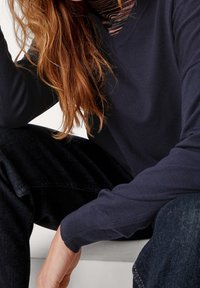 Pullover blu navy a V in tessuto knit con polsini a coste, abbinato a jeans scuri. La texture appare morbida e leggermente aderente.