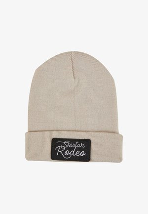 Kreminė megzta kepurė su sulenkta briauna. Pasižymi stačiakampiu juodu pleistru su balta užrašu "Skistar Rodeo". Minkšta tekstūra ir šiltas dizainas.