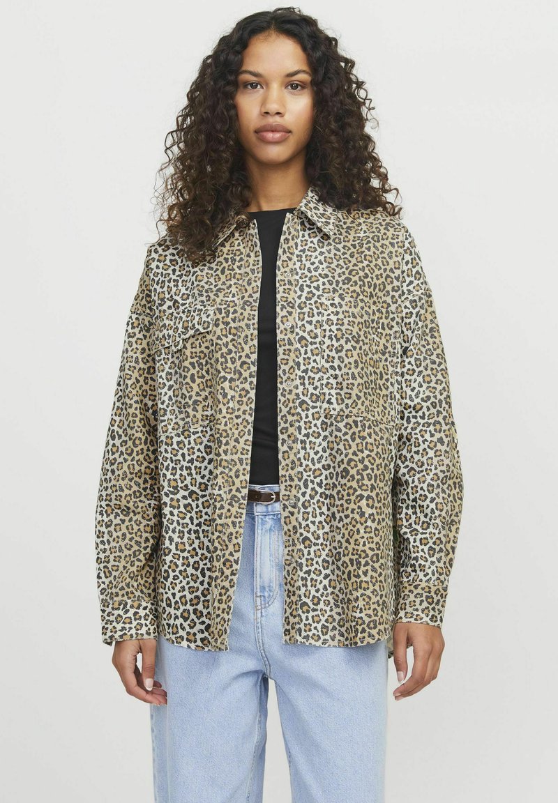 Leoprint Hemd in Beige und Schwarz mit Kragen und langen Ärmeln, kombiniert mit hellblauen Jeans.