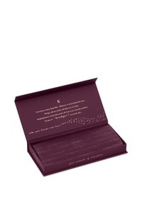 Offene dunkelviolette Schachtel mit goldener Schrift enthält ein gefaltetes Tuch oder eine Maske, die Luxus und Entspannung für die Augenpflege bewirbt.