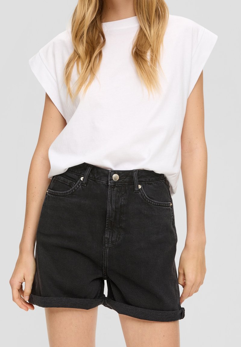 Zwarte denimshorts met een hoge taille, omgeslagen mouwen en voorzakken, gecombineerd met een losvallend wit t-shirt. Gladde textuur.