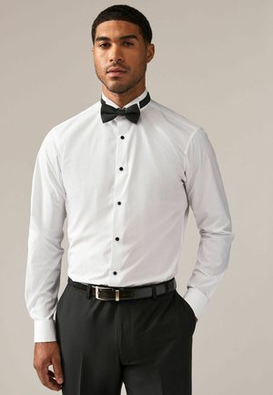 Cămașă albă cu nasturi negri și papion; pantaloni negri și curea; material neted; croi ajustat; design modern al gulerului.