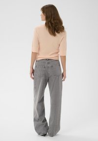 Helles rosa ribbeltes Strickoberteil und lässige graue Denim-Hosen mit hoher Taille, weitem Bein und aufgesetzten Taschen auf der Rückseite.