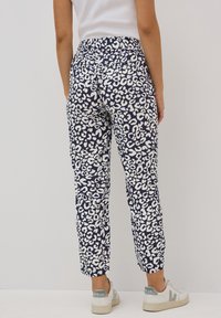Pantaloni stampati blu con un motivo leopardato bianco, vita elastica e design a gamba affusolata, abbinati a sneakers di colore chiaro.