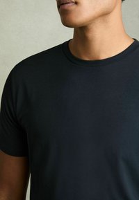 Tricou din bumbac negru, cu guler rotund, mâneci scurte, textură netedă și fără modele sau logo-uri vizibile. Prim-plan al gulerului și părții superioare a pieptului.