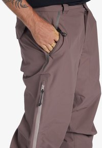 Pantalons légers et respirants pour hommes en marron discret, dotés d'une poche latérale avec fermeture éclair et de détails à cordon pour un ajustement personnalisé.
