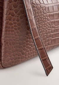 Sac à main en cuir marron avec texture crocodile et une sangle assortie posés en diagonale sur une surface claire.