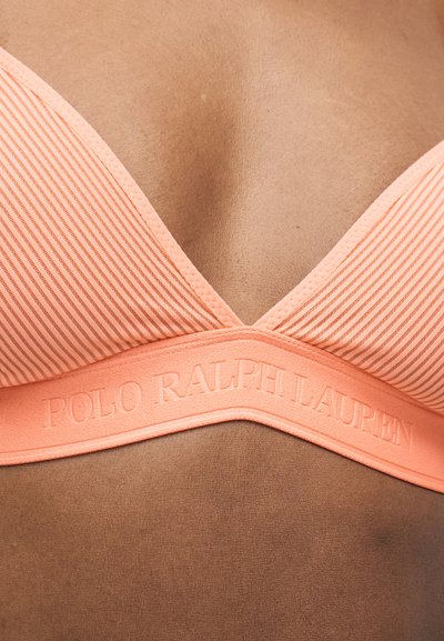 Κοντινό πλάνο σε σουτιέν ριγέ χρώματος ροδάκινου με χαραγμένο το όνομα «Polo Ralph Lauren» στη λωρίδα, που φοριέται στο στήθος ενός ατόμου.