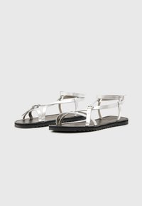Zilveren metallic sandalen met meerdere banden, zwarte gestructureerde zool, enkelsluiting en open ontwerp voor ademend vermogen.