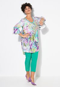 Flerfärgad tunika med blommönster, bell sleeves och V-ringning, i kombination med gröna smala byxor och lila klackar. Detalj med silverhandväska.