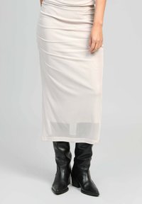Jupe midi ajustée couleur crème avec des détails de fronces et une couche inférieure transparente, associée à des bottes en cuir noir à hauteur de genou avec des talons épais.