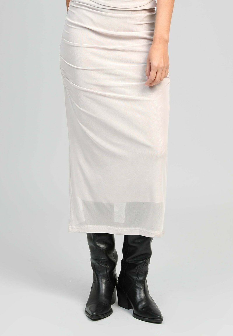 Jupe midi ajustée couleur crème avec des détails de fronces et une couche inférieure transparente, associée à des bottes en cuir noir à hauteur de genou avec des talons épais.