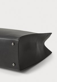 Zwarte rechthoekige tas van glad materiaal, met afgeronde hoeken, metalen studs aan de onderkant en een licht gestructureerd ontwerp.