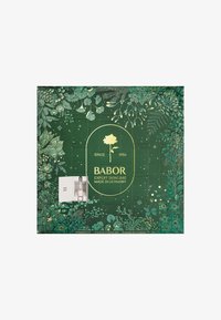 Green advent calendar with floral design, gold accents, and 24 numbered doors. Contains a visible ampoule in a white box labeled "Huid push."