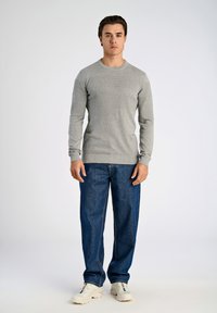 Ljust grå stickad tröja med texturerade horisontella ränder, tillsammans med lösa blå jeans och vita sportskor.