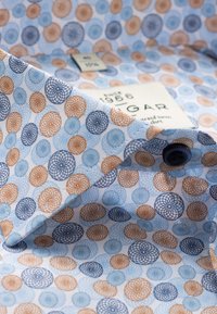 Overhemd met blauwe, oranje en marineblauwe cirkelpatronen op een lichte achtergrond. Bevat een label en donkere knoopdetails op de kraag.