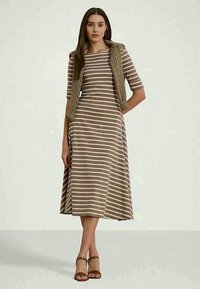 Δ striped φόρεμα σε μπεζ και κρέμα, με κοντά μανίκια, εφαρμοστό κορσέ και φαρδιά φούστα. Φορεμένο με ένα υφασμένο, πλεκτό γιλέκο.