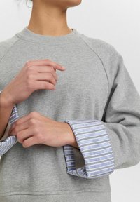 Grå sweatshirt med ribbad halsringning, med blå och vita randiga mudd. Mjuk textur, avslappnad design och ledig passform.