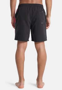 Μαύρο μαγιό σορτς με ελαστική ζώνη μέσης, πλαϊνές τσέπες και πίσω τσέπη. Διακριτικές κόκκινες και λευκές ρίγες στα πλαϊνά. Ελαφρύ ύφασμα.