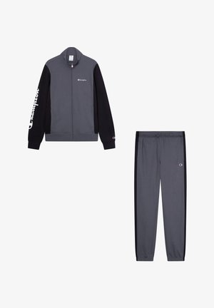 Grijze trainingspak met een ritsjack met zwarte mouwen en een logo. Broek met zwarte zijstrepen en een elastische tailleband. Zacht materiaal.