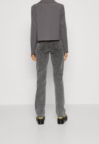 Blazer grigio corto con collar a revers, indossato su jeans grigi a gamba larga con tasche e cuciture visibili, abbinato a stivali platform neri.
