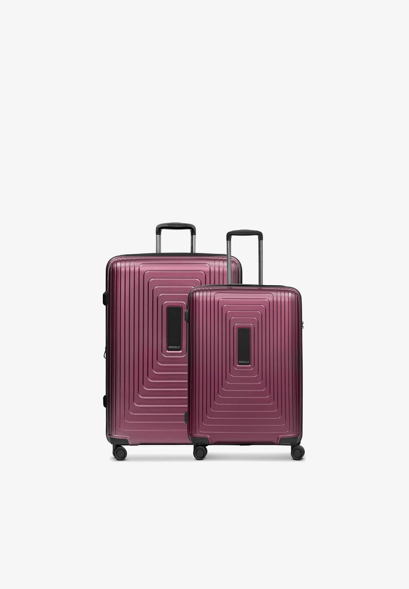 Deux valises rigides bordeaux de tailles différentes avec poignées télescopiques et quatre roues pivotantes sur fond blanc.