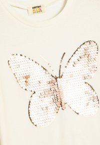 Maglietta per bambini color beige chiaro con un grande design di farfalla realizzato in paillettes scintillanti nelle tonalità di rosa e oro.