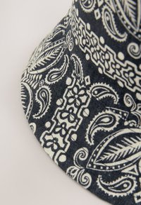 Cappello a secchiello nero con motivo paisley bianco, realizzato in cotone con una finitura testurizzata e una tesa cucita per una maggiore struttura.