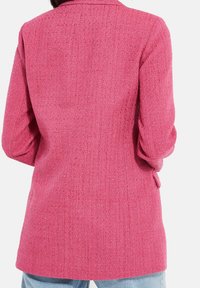 Blazer rose texturé à manches longues, col à cran, et deux poches latérales, avec un motif tissé subtil et une coupe ajustée.