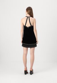 Abito halter in velluto nero con una silhouette aderente, adornato da borchie decorative lungo il colletto e l'orlo, con una schiena scoperta dal design ritagliato.
