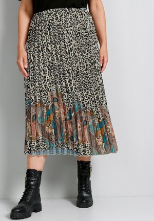 Person wearing a leopard print midi skirt with a colorful paisley border and black lace-up combat boots, standing on a gray floor.