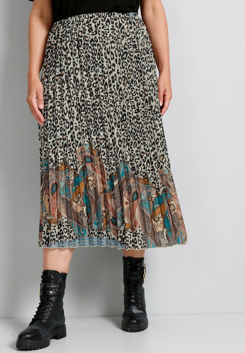 Personne portant une jupe midi à imprimé léopard avec une bordure cachemire colorée et des bottes de combat noires à lacets, debout sur un sol gris.