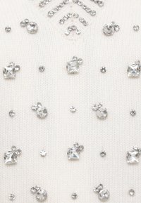 Maglione color crema con rhinestones argentati disseminati in varie forme e dimensioni, caratterizzato da un motivo lavorato sotto il colletto.