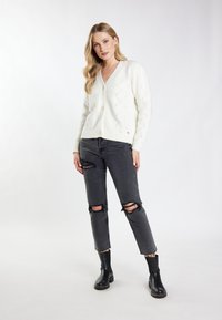 Cardigan bianco lavorato a maglia con scollatura a V, chiusura a bottoni e motivo a rombi. Abbinato a jeans neri strappati e stivaletti neri alla caviglia.