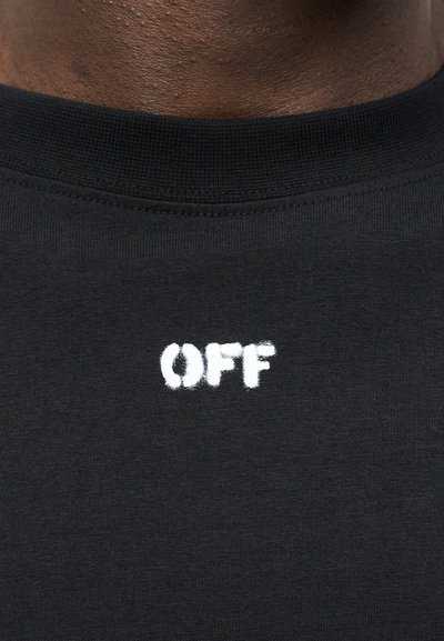 Κοντινό πλάνο μαύρου μπλουζιού με στρογγυλή λαιμόκοψη και λευκό κείμενο "OFF" κεντραρισμένο κάτω από τη λαιμόκοψη σε σκούρο δέρμα.