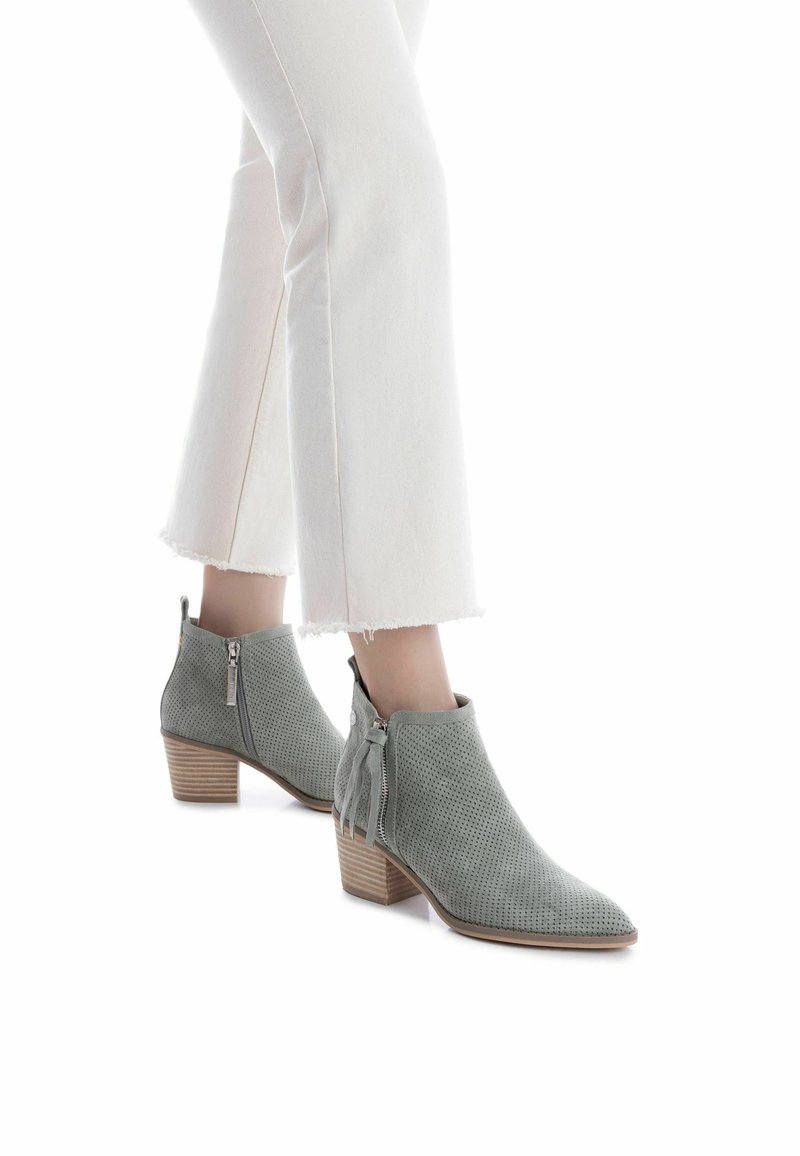 Botines grises perforados con punta puntiaguda y tacón cuadrado, con cremalleras laterales y detalles de borlas. Combinados con jeans blancos de dobladillo deshilachado.