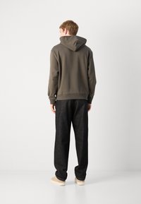 Felpa con cappuccio in oliva scuro con polsini a costine, abbinata a pantaloni larghi grigio scuro. Tessuto morbido con una vestibilità rilassata e dettagli minimi.