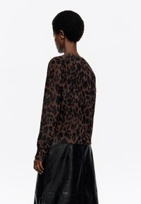 Suéter con estampado de leopardo marrón y negro, con una textura suave, mangas largas y un escote redondeado, combinado con una falda de cuero negra.