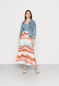 Jaqueta de ganga, top cropped azul claro e uma saia longa com padrões ondulados em coral, azul e branco. Sandálias de salto bloco azuis completam o visual.