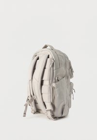 Ανοιχτό γκρι σακίδιο με επενδεδυμένους ιμάντες, πολλαπλά διαμερίσματα με φερμουάρ και πλαϊνές τσέπες, όρθιο σε λευκό φόντο.