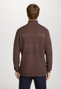 Bruine gebreide trui met een hoge kraag, voorzien van een gestructureerd patroon en ribbels aan de mouwen. Het ontwerp bevat horizontale strepen en heeft een ontspannen pasvorm.