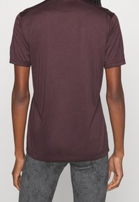 Camiseta atlética burdeos de manga corta, con textura suave y cuello redondo. Combinada con leggings grises texturizados.