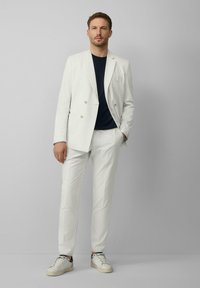 Lichtgrijs dubbelzijdig colbert met bijpassende broek, gecombineerd met een marineblauw T-shirt en witte sneakers, met subtiele textuur en een getailleerde pasvorm.