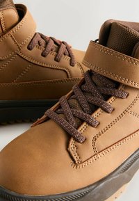 Braune Leder-Stiefeletten mit braunen Schnürsenkeln, gepolsterter Kante und strukturiertem Obermaterial. Mit verstärkten Nähten und strapazierfähiger Sohle.