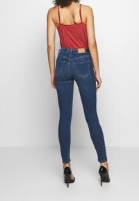 Jeans in denim blu slim con vita alta, dotati di tasche posteriori e dettagli di cucitura sottili. Abbinati a un top rosso aderente.