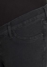 Detailní záběr osoby v černých džínech a černém topu, zaměřující se na pas, poutka na opasek a detaily přední kapsy.