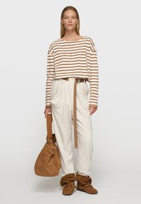 Gestreepte cropped top met lange mouwen in crème en bruin, gecombineerd met lichtcrème hoge taillebroek en een browngemaakt leren tote bag. Gelaagde schoenen.