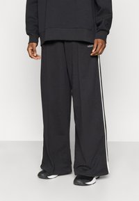 Crne široke trenirka hlače od mješavine pamuka, s bijelim bočnim prugama i izvezenim logotipom. Mekana tekstura, casual dizajn.