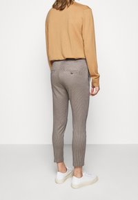 Beżowy sweter z długim rękawem w zestawieniu z brązowymi spodniami w kratę i białymi sneakersami. Spodnie posiadają tylne kieszenie z guzikami.